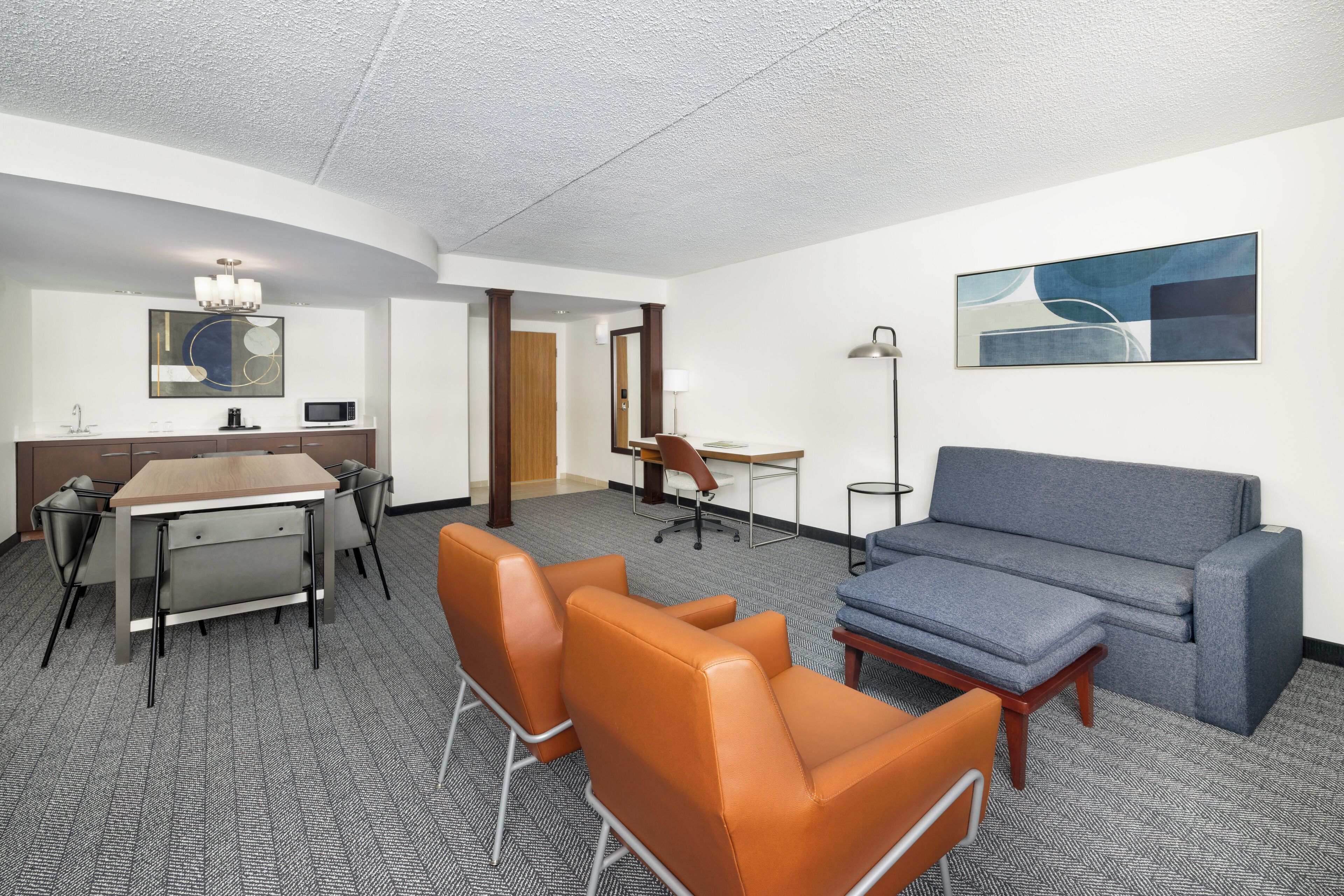 A hotel room with a dining table, two chairs, a sofa, a desk, and a lamp.