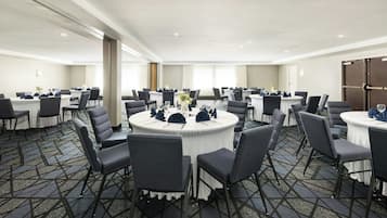 Un salón de conferencias con mesas redondas, sillas y piso alfombrado.