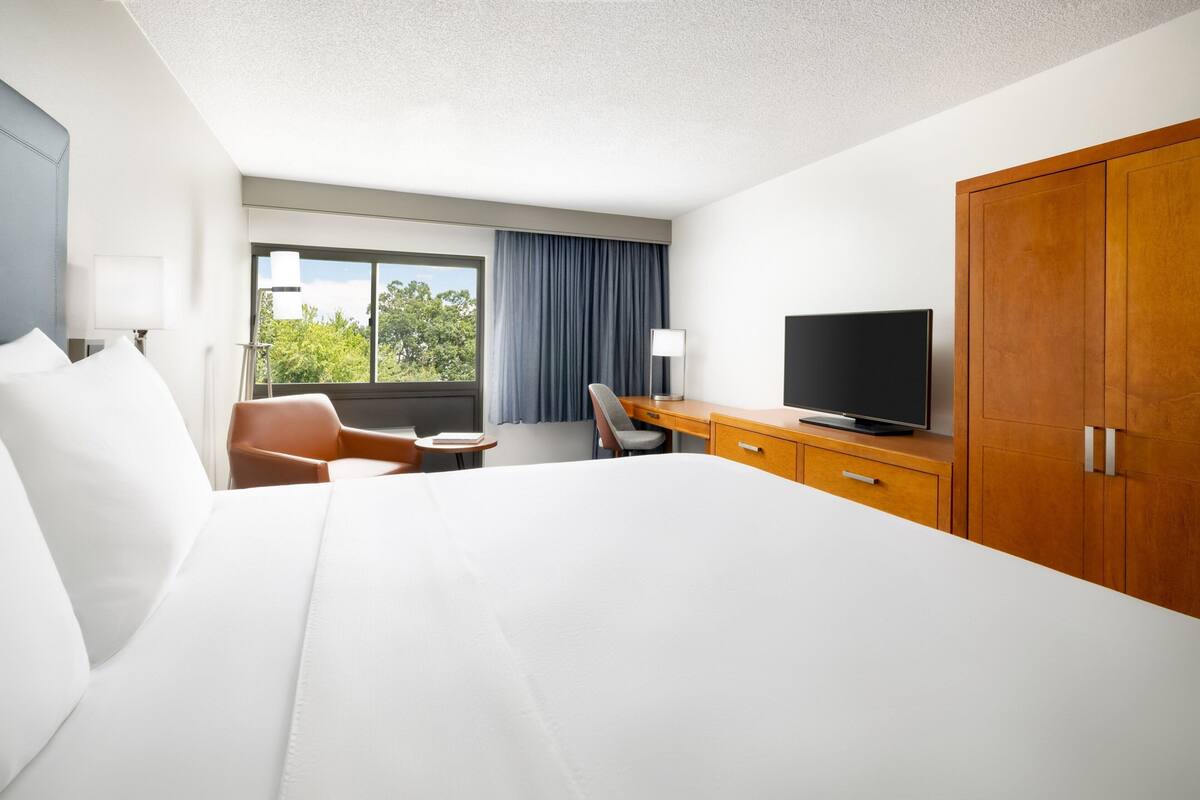 A hotel room with a large bed, a desk with a television, a chair, and a window with curtains.