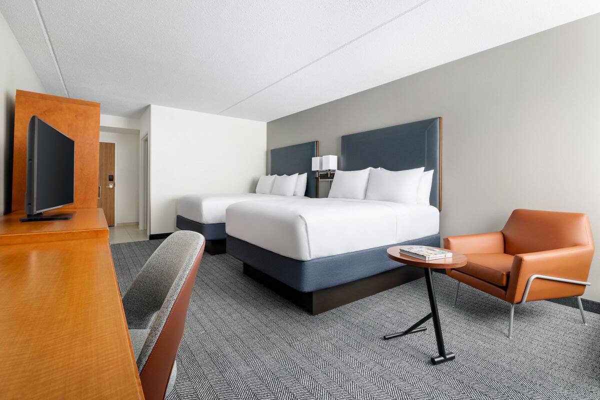 A hotel room with a large bed, a desk, a chair, and a small table.