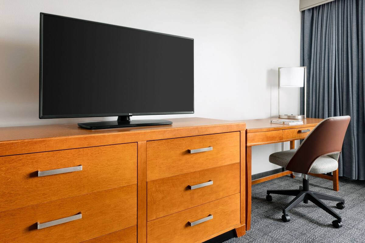 A hotel room with a wooden desk, a flat-screen TV, a lamp, and a chair.