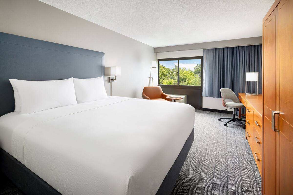 A hotel room with a large bed, a desk, a chair, and a wardrobe.