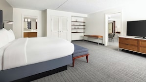 A hotel room with a large bed, a desk, a television, a bookshelf, and a bathroom visible through an open door. - Courtyard by Marriott Montvale (Montvale)