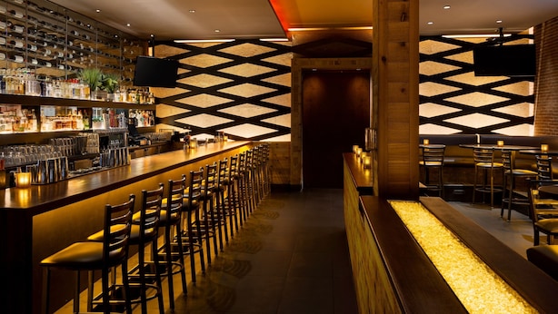A bar area with a long counter, multiple bar stools, and a wall-mounted TV. - Courtyard by Marriott Montvale (Montvale)