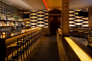 A bar area with a long counter, multiple bar stools, and a wall-mounted TV.