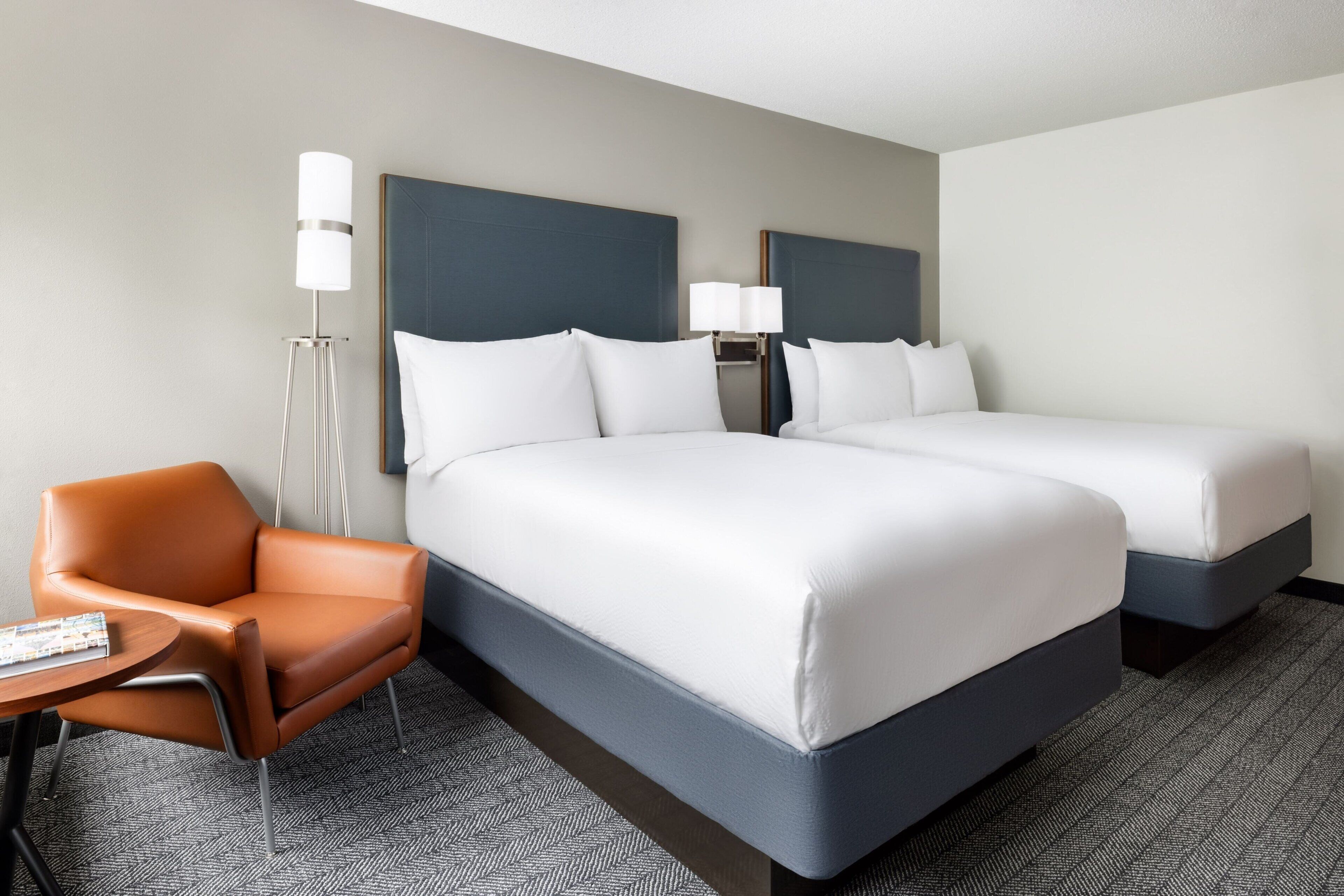 Ein Hotelzimmer mit zwei Betten, einem Sessel, einem kleinen Tisch und einer Lampe.