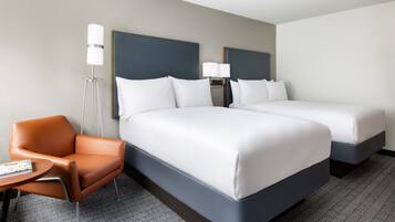 Ein Hotelzimmer mit zwei Betten, einem Sessel, einem kleinen Tisch und einer Lampe.