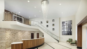 A spacious lobby with a reception desk, a staircase, and a large window with a forest view. - Courtyard by Marriott Montvale (Montvale)