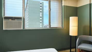 Una camera d'albergo con un letto, una finestra con persiane, un condizionatore, una lampada e una sedia.