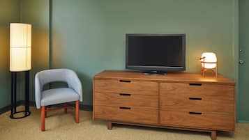 A room with a wooden dresser, a television on top, a lamp, and a chair.
