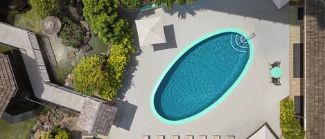 An aerial view of a swimming pool surrounded by lounge chairs and umbrellas, with a small fountain and greenery.