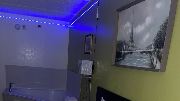 A hotel room with a bed, a bathtub, and a painting of a bridge. - Willow Lodge Willoughby – Cleveland Mentor (Willoughby)