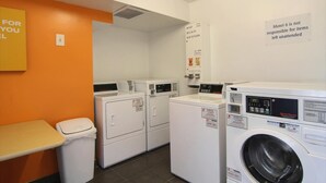 A laundry room with multiple washing machines and dryers, a trash bin, and a sign indicating the room is for guests. - Willow Lodge Willoughby – Cleveland Mentor (Willoughby)