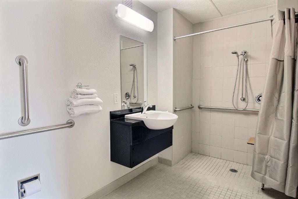 A bathroom with a white sink, a mirror, a towel rack, and a shower area.