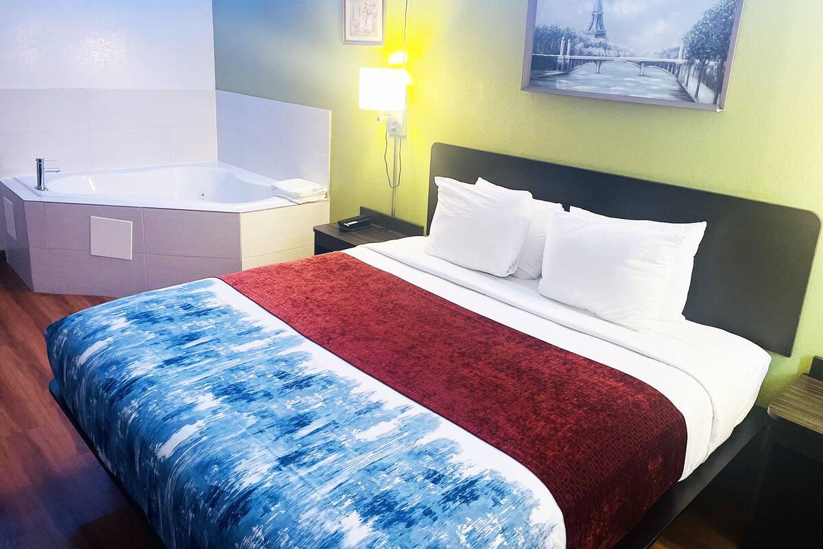 Ein Hotelzimmer mit Bett, einem großen Fenster, einem Gemälde vom Eiffelturm und einem Badezimmer mit Badewanne.