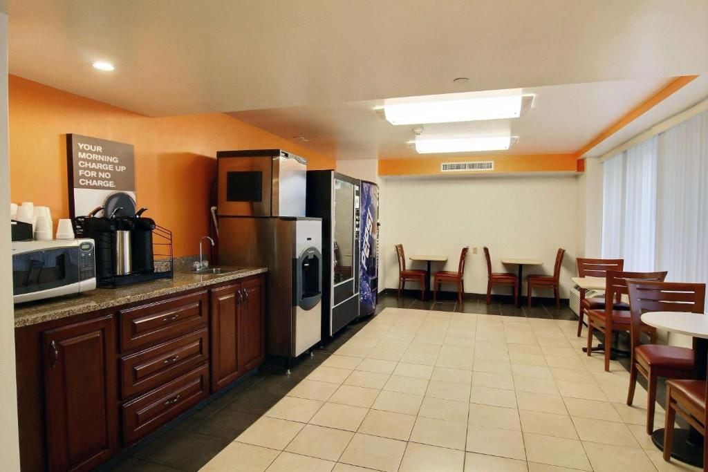 A hotel kitchen with a microwave, coffee maker, refrigerator, and a sign about morning charge.