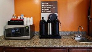 Une cuisine équipée d’un four à micro-ondes, d’une machine à café et d’un panneau indiquant les tarifs pour la recharge des appareils électroniques le matin.