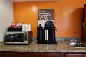 A kitchen with a microwave, coffee maker, and a sign about morning charge.