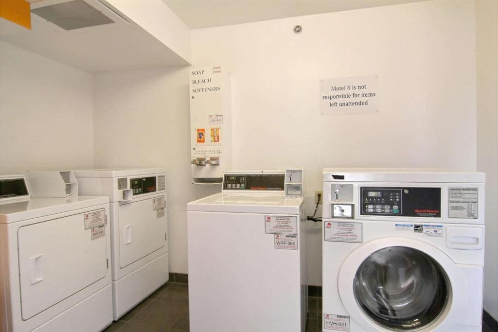 A laundry area with three white washers and dryers, a sign about soap and bleach, and a notice about unattended items.