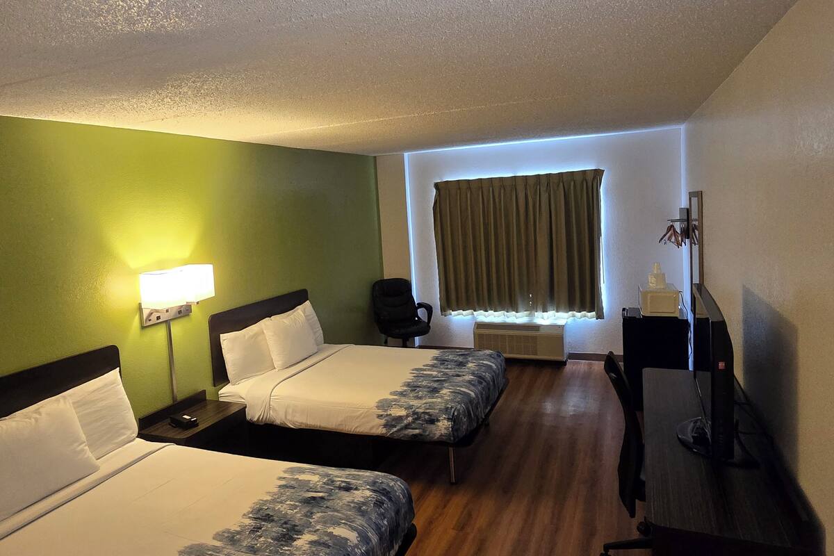 Ein Hotelzimmer mit zwei Betten, einem Schreibtisch, einem Stuhl, einer Lampe und einem Fenster mit Vorhängen.