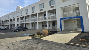 A multi-story hotel with a 'Welcome' sign, parking spaces, and a landscaped area with plants. - Willow Lodge Willoughby – Cleveland Mentor (Willoughby)