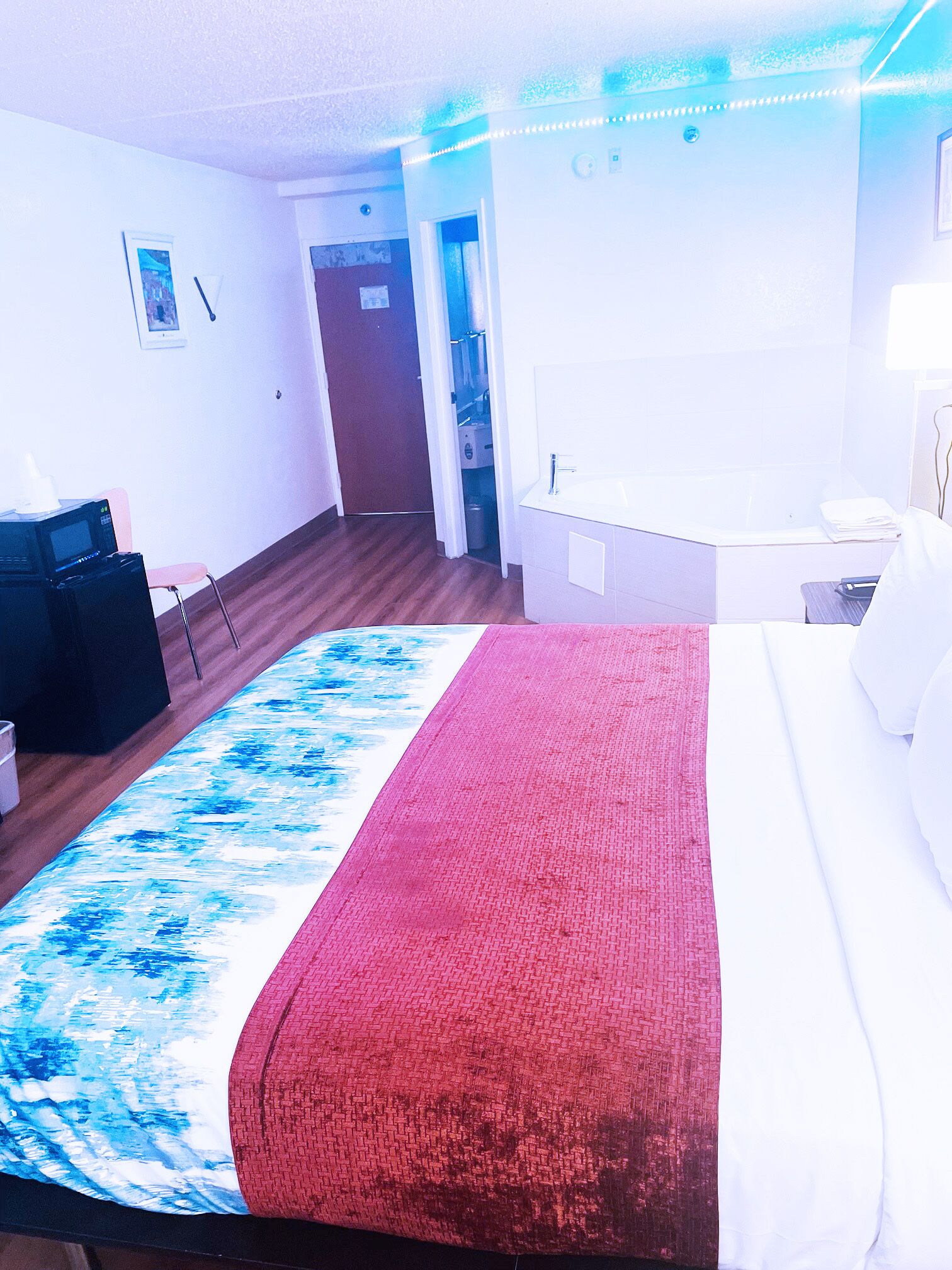A hotel room with a bed, a desk, a chair, a microwave, a trash bin, and a bathroom door.