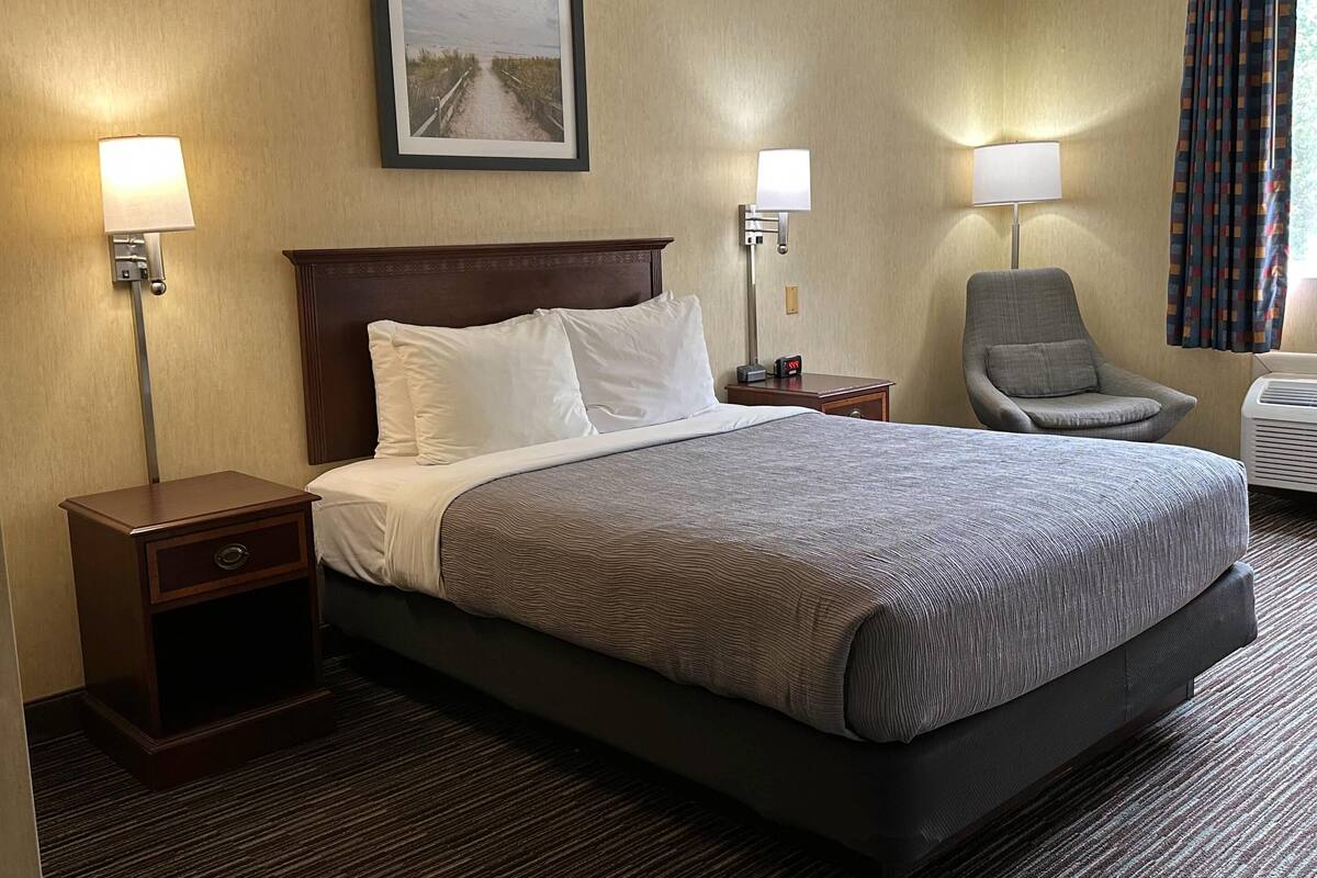 A hotel room with a large bed, two bedside tables, a chair, a picture on the wall, and a window with curtains.