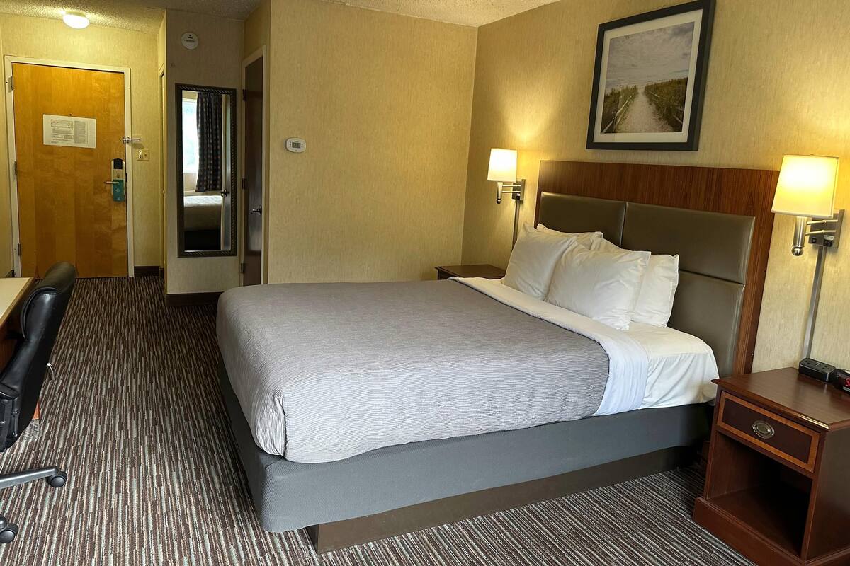 A hotel room with a bed, bedside tables, a desk, and a chair.