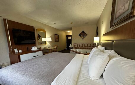 A hotel room with a large bed, a desk, a chair, a small table, a lamp, a TV, and a bathroom with a bathtub.