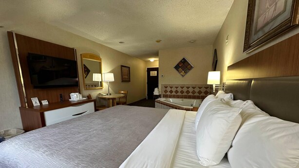 A hotel room with a large bed, a desk, a chair, a small table, a lamp, a TV, and a bathroom with a bathtub. - Quality Inn near Toms River Corporate Park (Manchester Township)