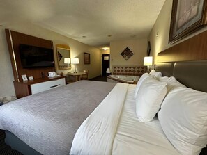 Habitación de hotel con una cama grande, un escritorio, una silla, una mesita, una lámpara, un televisor y un baño con bañera.