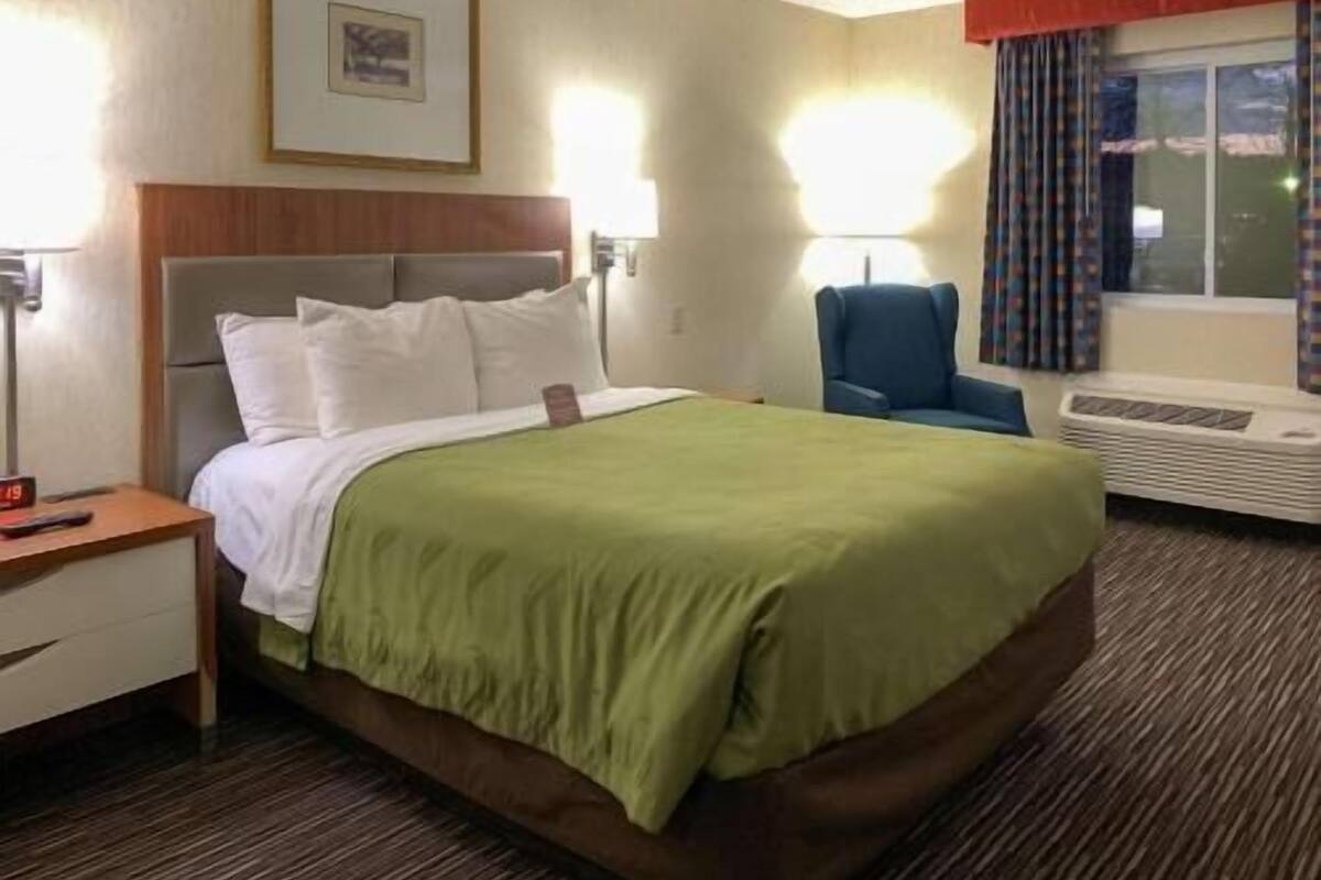 A hotel room with a bed, a chair, a desk, and a window with curtains.