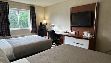 A hotel room with two beds, a desk with a computer, a TV, and a window with curtains.