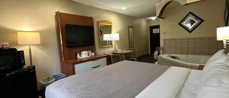 Habitación de hotel con una cama grande, un escritorio con televisor de pantalla plana, una lámpara de escritorio, un espejo, un teléfono, un cubo de basura y una bañera.