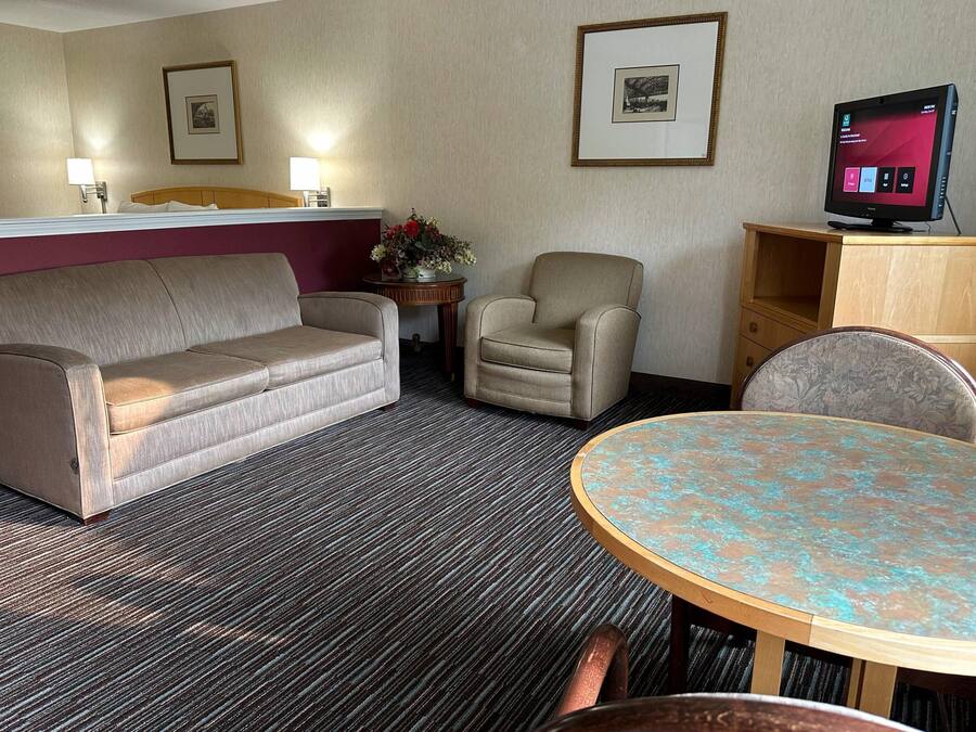 A hotel room with a sofa, armchair, small table, and a TV on a stand.