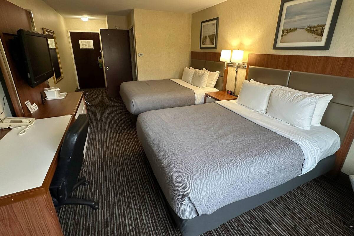 A hotel room with two beds, a desk with a telephone, a chair, a TV, and two lamps.