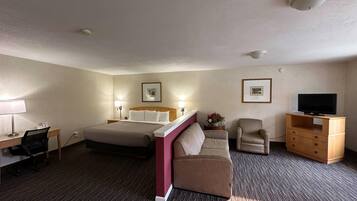Habitación de hotel con cama, escritorio con silla, sofá, mueble para televisión y dos lámparas de pared.
