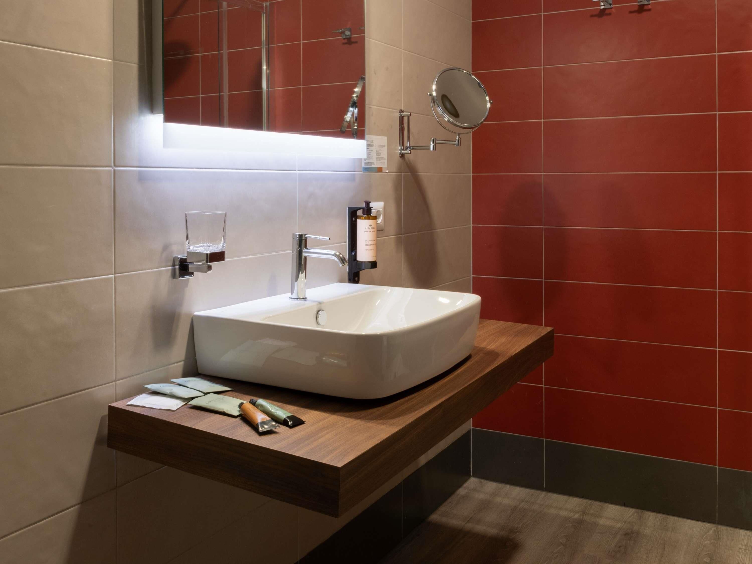 A modern bathroom with a white sink, a mirror, and a wooden vanity.