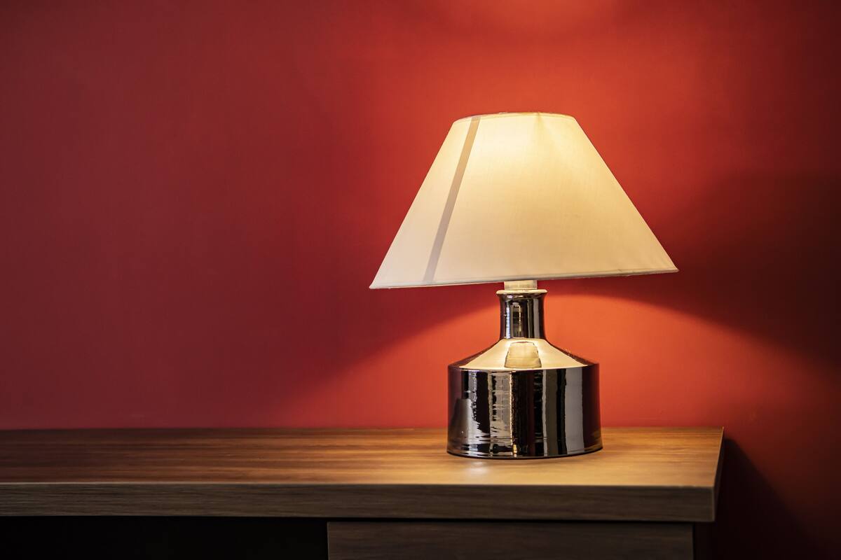 A table lamp with a white shade on a wooden surface against a red wall.