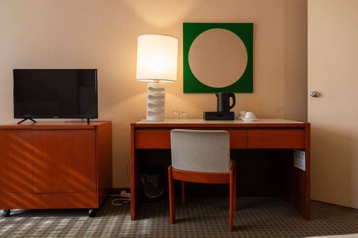 Habitación de hotel con televisión, lámpara, cafetera, silla y escritorio.