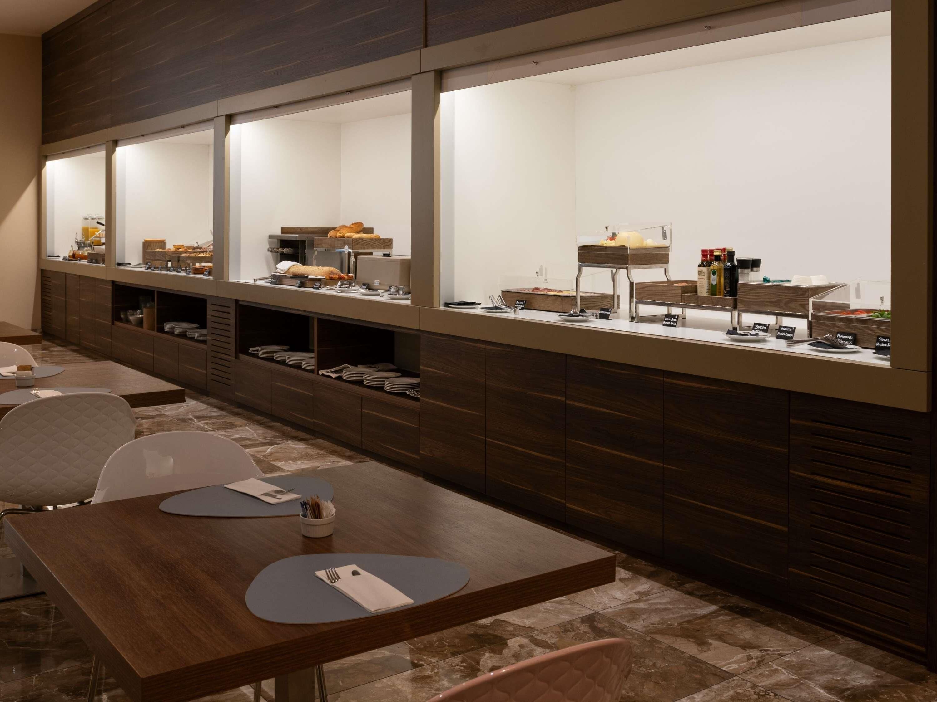 A modern breakfast area with a long counter, multiple seating options, and a variety of food and drink dispensers.