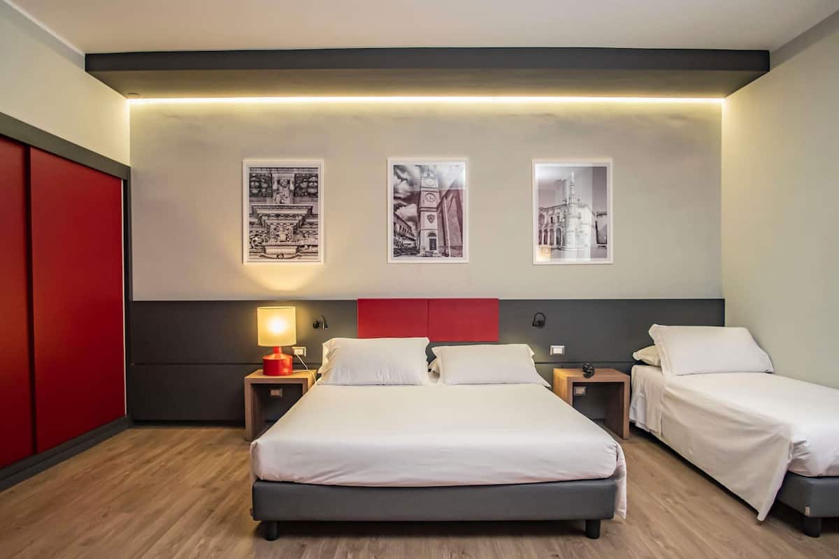 A hotel room with two single beds, a red accent wall, and three framed pictures on the wall.