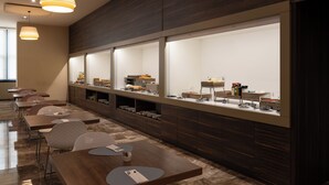 A modern hotel room with a long dining table, multiple chairs, and a buffet counter.
