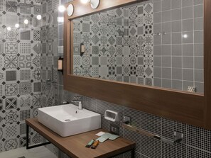 A bathroom with a white sink, a wooden vanity, a large mirror, and patterned tiles.