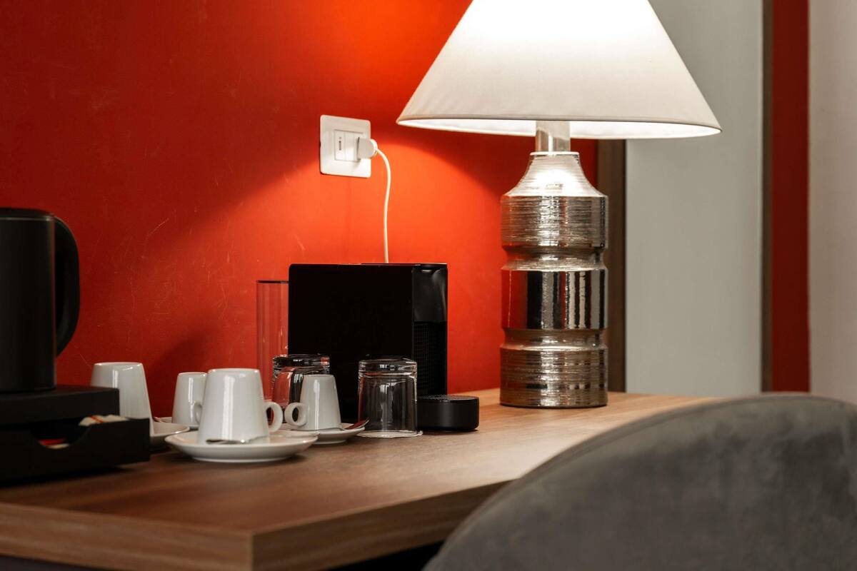 A hotel room with a wooden desk, a lamp, a coffee maker, and a power outlet.