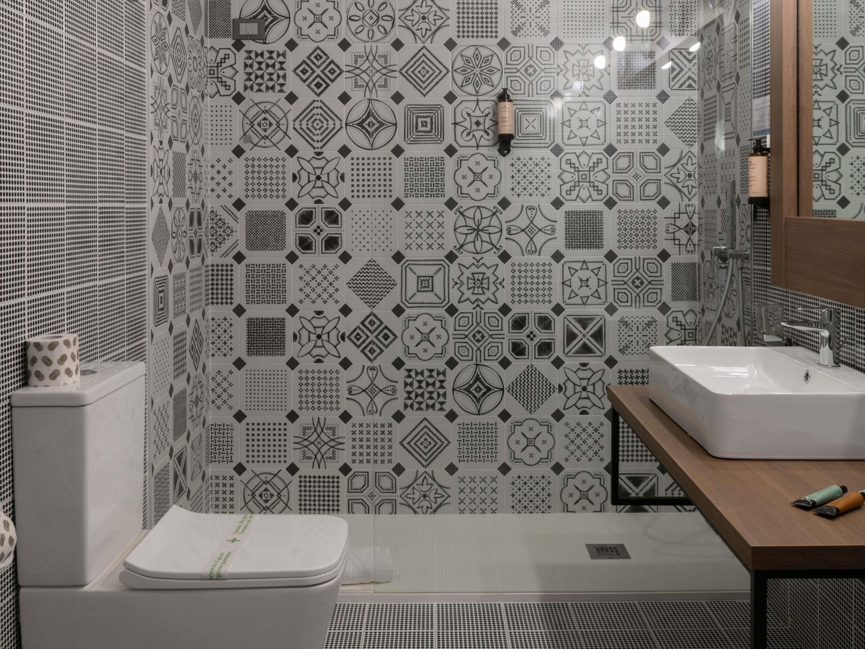 A modern bathroom with patterned tiles, a toilet, a sink, and a shower.