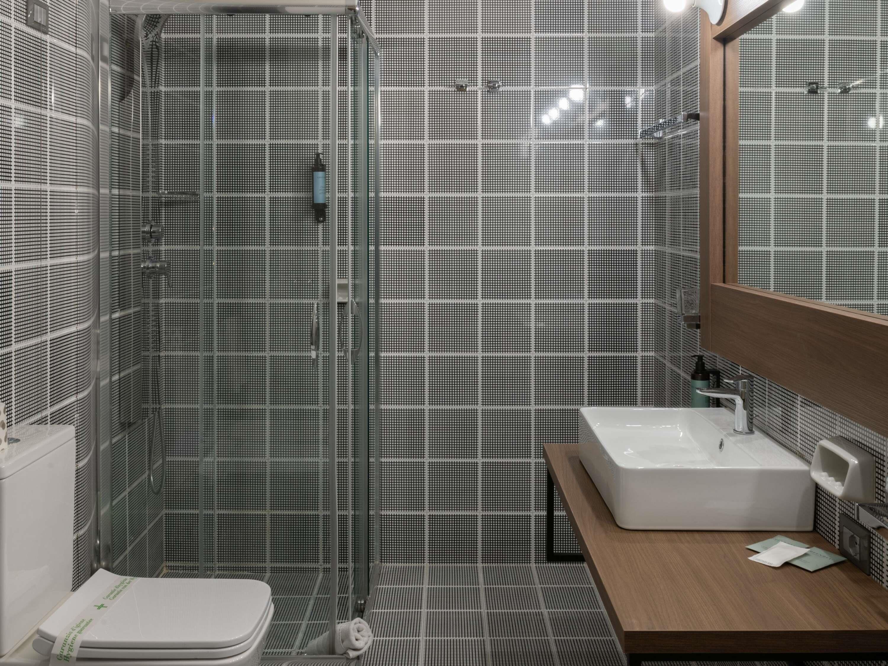 A modern bathroom with a glass-enclosed shower, a white sink, and a wooden vanity.