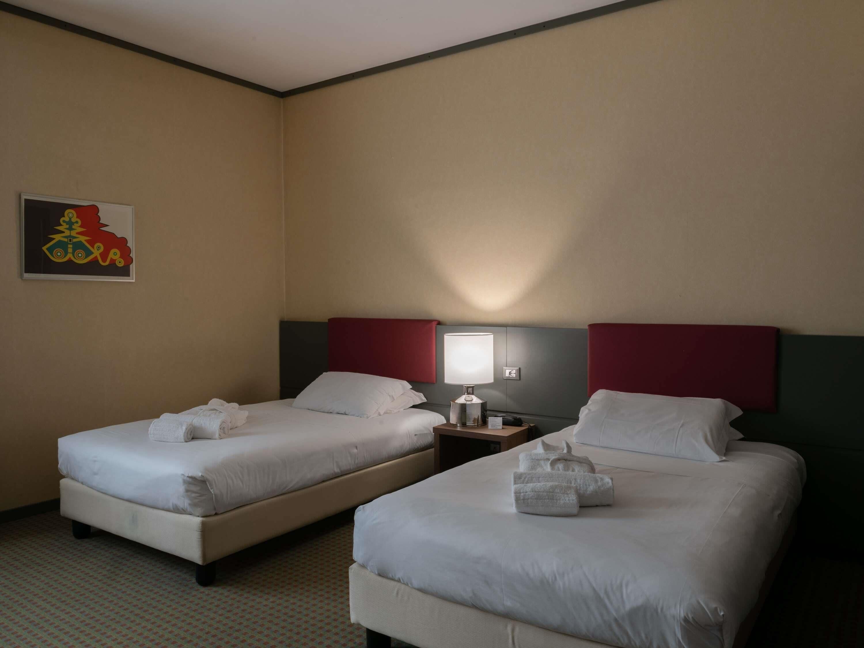 Habitación de hotel con dos camas, una mesita de noche, una lámpara y una obra de arte colgada en la pared.