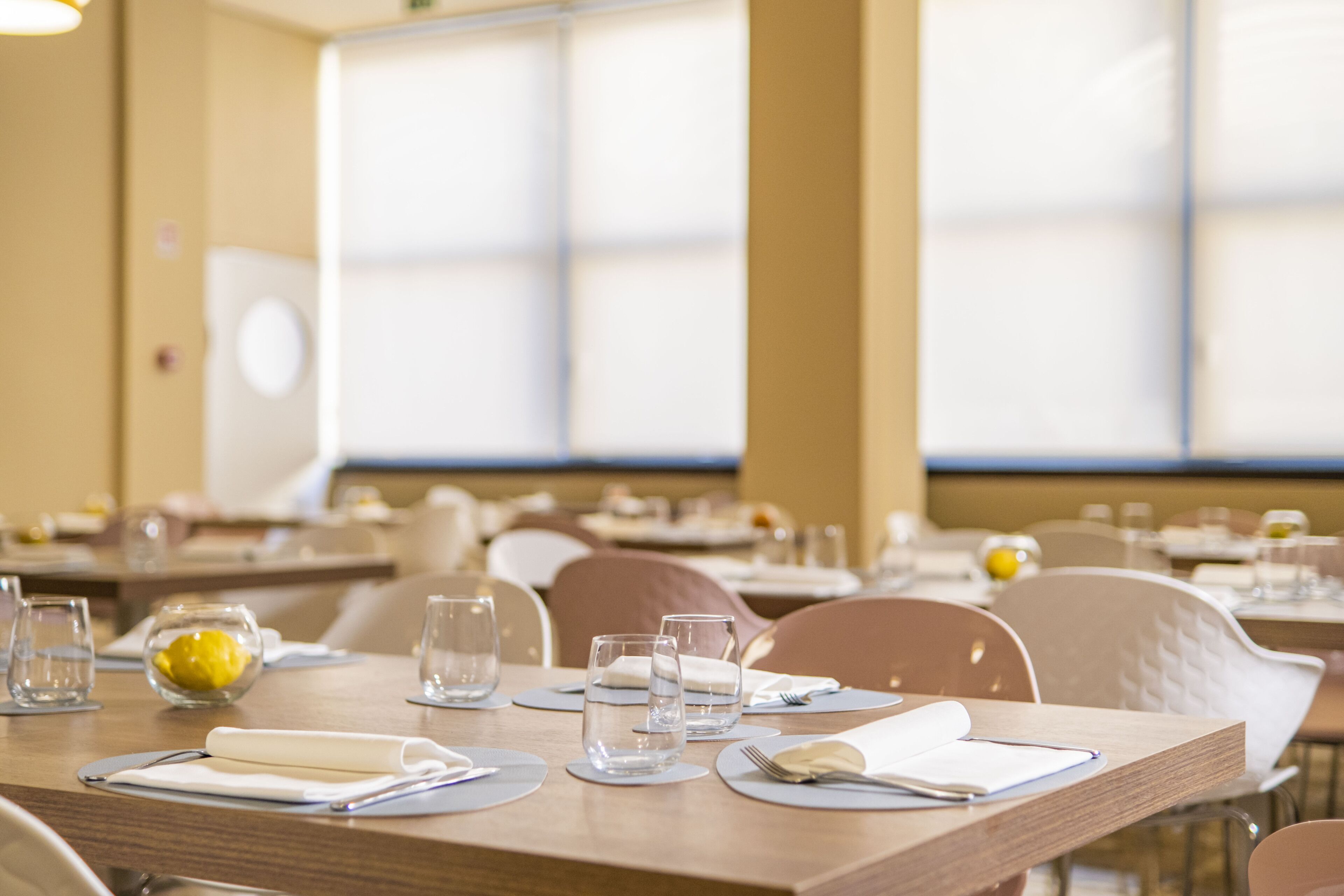 Un espace repas avec des tables dressées, de la vaisselle transparente et un citron posé sur la table.