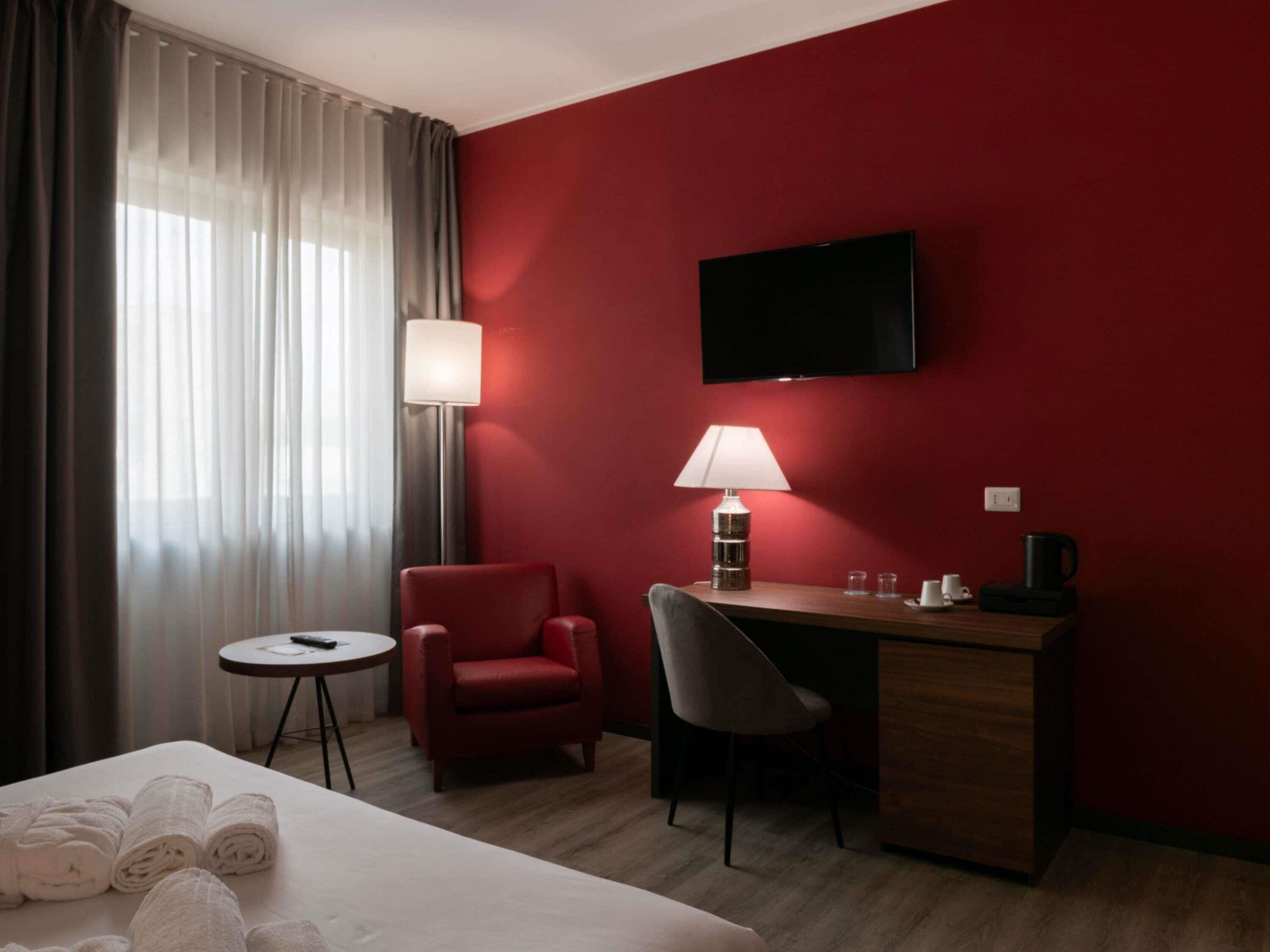 A hotel room with a bed, a desk, a chair, a TV, a lamp, a coffee maker, and a small table with towels.